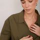 Close-up of model's hands adjusting the neckline of the khaki shirt.