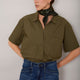 Model wearing khaki short-sleeved shirt with a printed scarf, tucked into blue jeans.