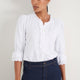Model wearing a crisp white cotton blouse with scalloped frill details.