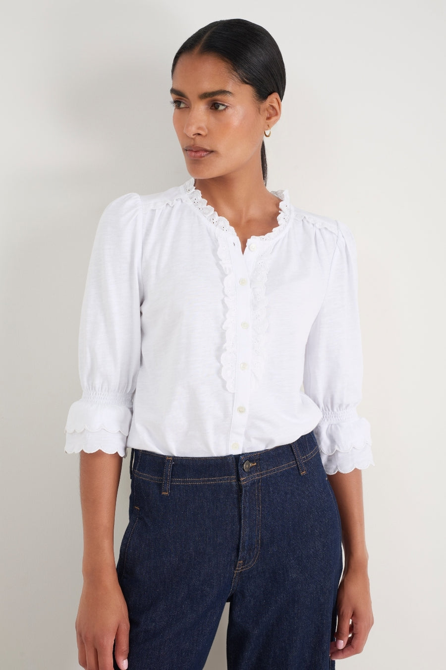 Model wearing a crisp white cotton blouse with scalloped frill details.