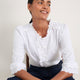 Model sitting wearing white cotton blouse and blue jeans.