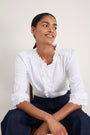 Model sitting wearing white cotton blouse and blue jeans.