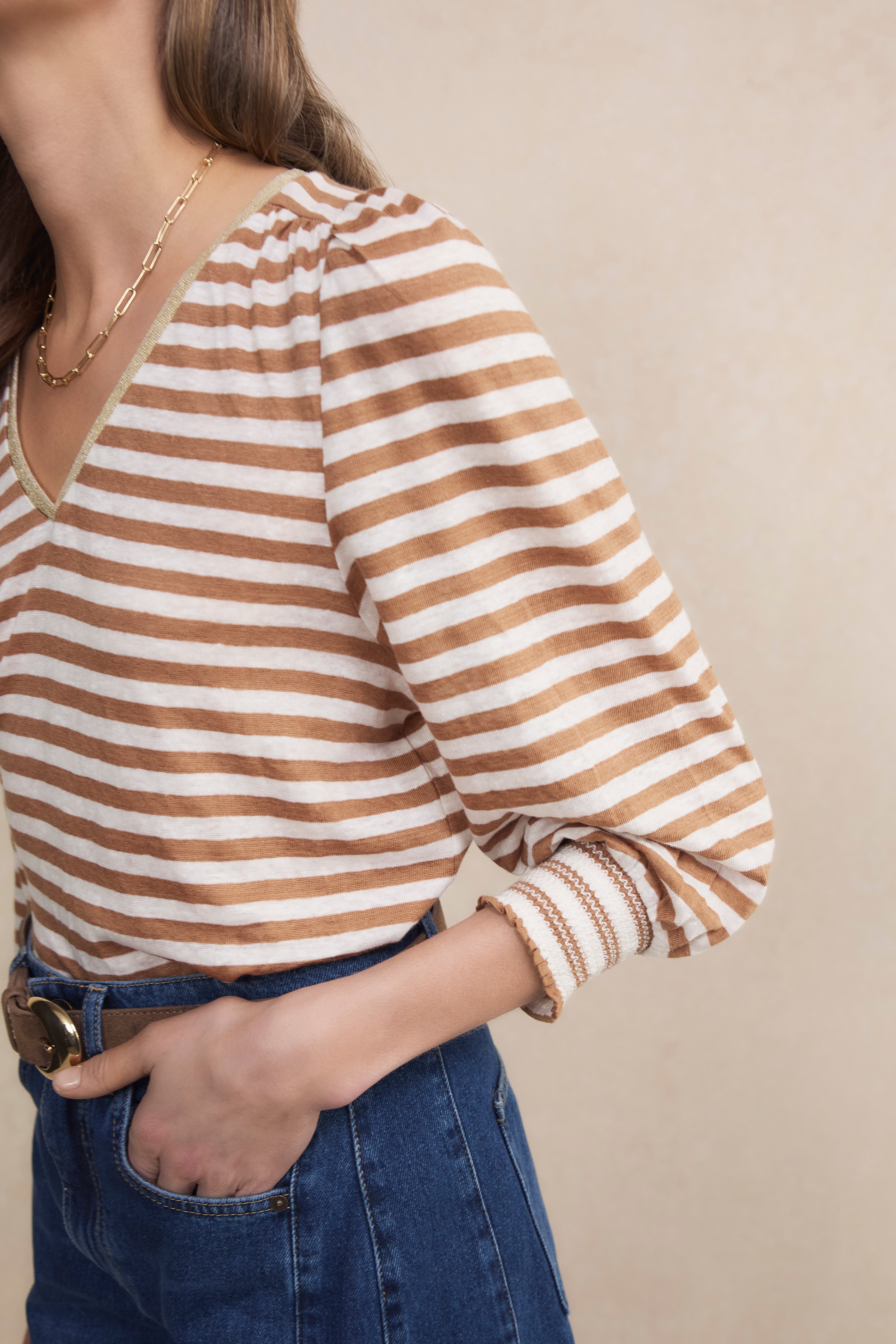 Person wearing a brown and white striped shirt with blue jeans on a beige background