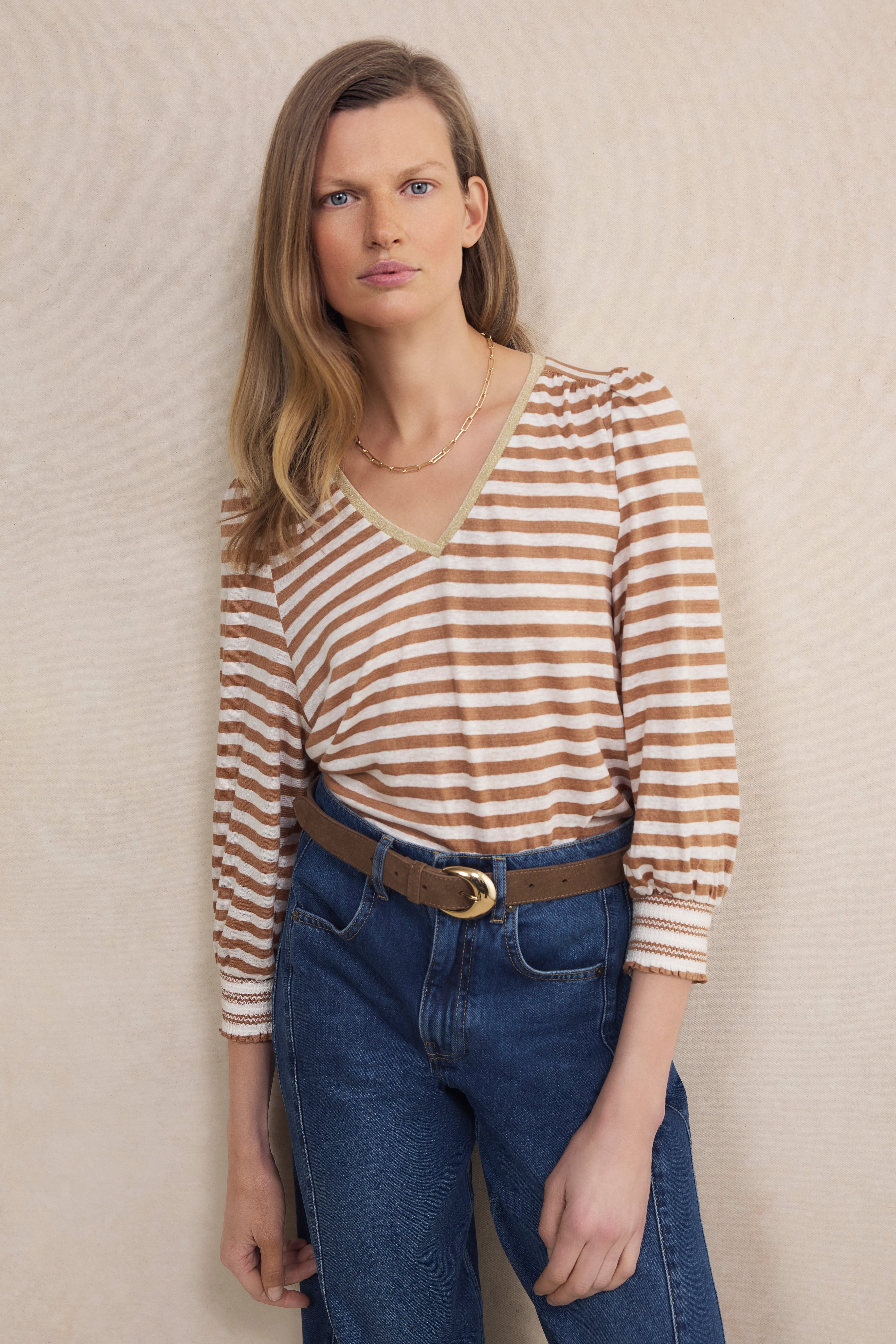 Woman wearing a striped shirt and blue jeans against a beige wall