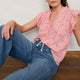 Woman sitting wearing pink embroidered Talya top with ruffle shoulders