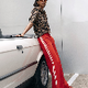 A woman posing next to a white car, wearing a leopard-print top and bright red track pants with white side stripes.
