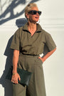 Model in khaki shirt and khaki trousers holding a clutch bag.